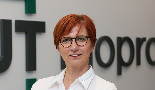Referenzkunde_1_GSI_Claudia-Kropp-600x347_76-1 eine rotharige Personalreferentin mit Brille vor einem Firmenlogo